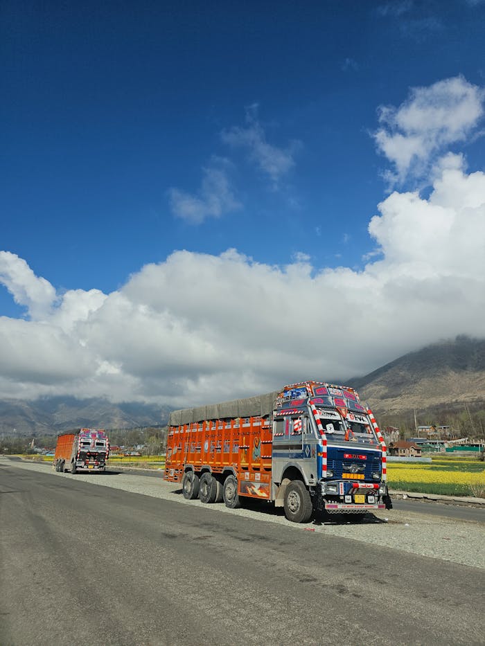 Vibrantly painted trucks on a scenic mountain road with bright blue skies and puffy clouds.