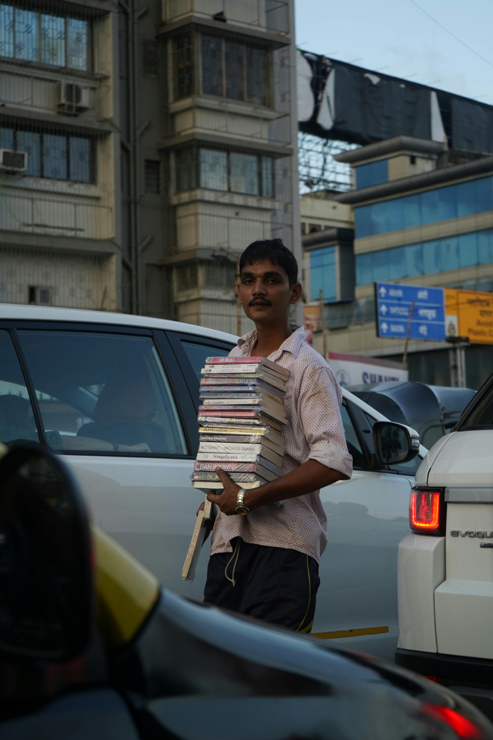 A man selling books among cars in a bustling urban street, capturing a slice of city life.